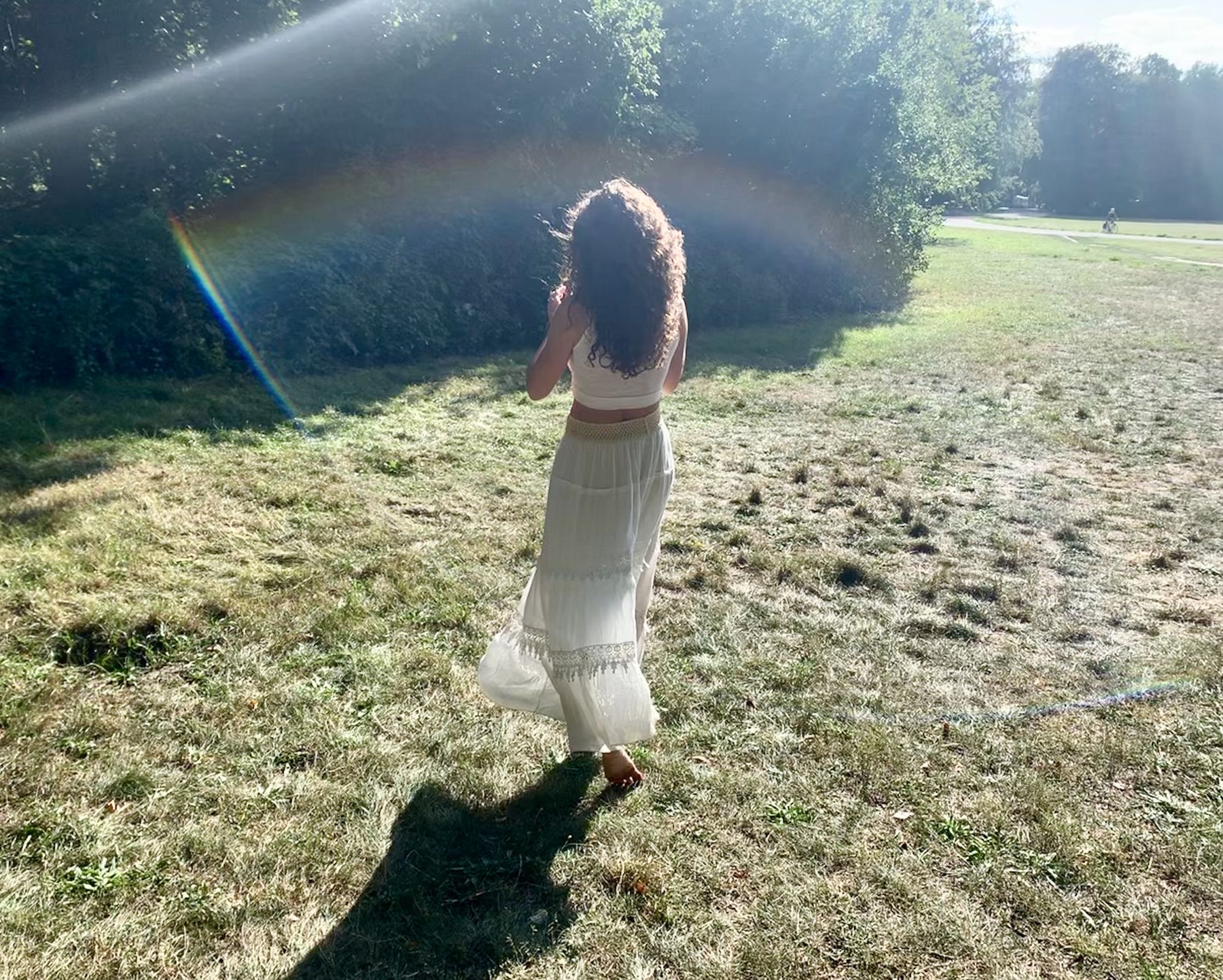 lisa walking through a sunlit park in a flowing white boho outfit